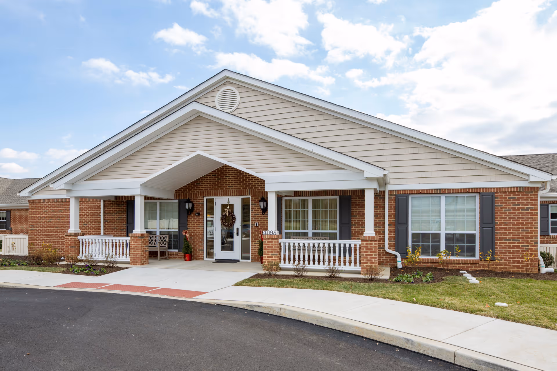 Front entrance of a single-story brick senior living building with a covered porch, white columns, and double glass doors.