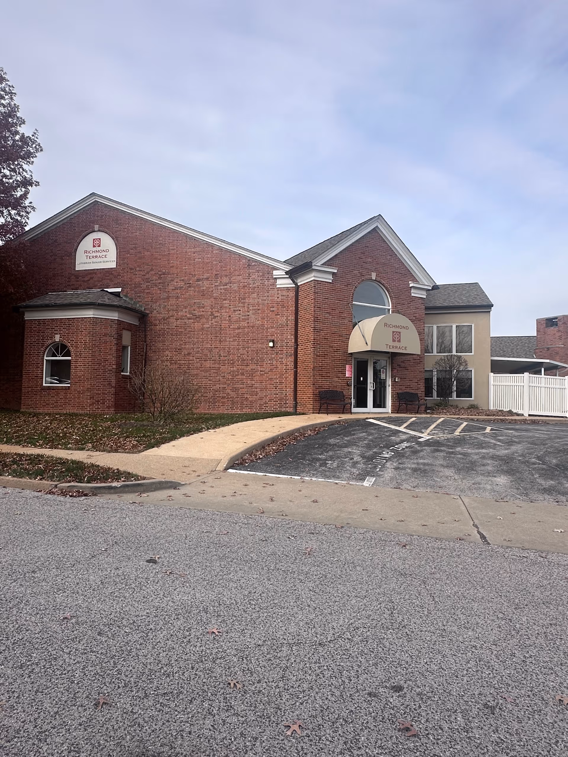 Brick front entrance of the Richmond Terrace senior living facility with a small parking area and walkway.