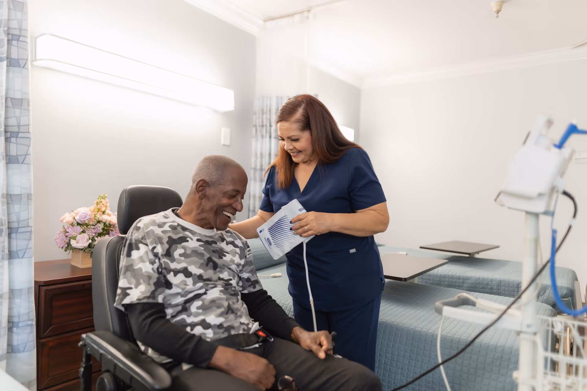 A senior man smiles while a caregiver takes his blood pressure in a healthcare facility room.