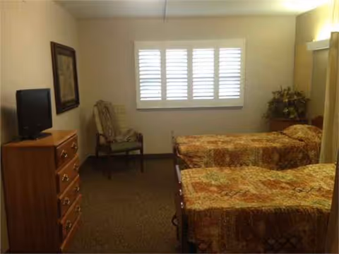 Two single beds with matching quilts, a dresser, chair, and window with shutters.