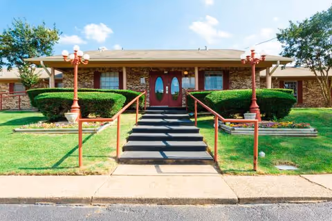 Front entrance of a senior living facility with red doors and manicured landscaping.