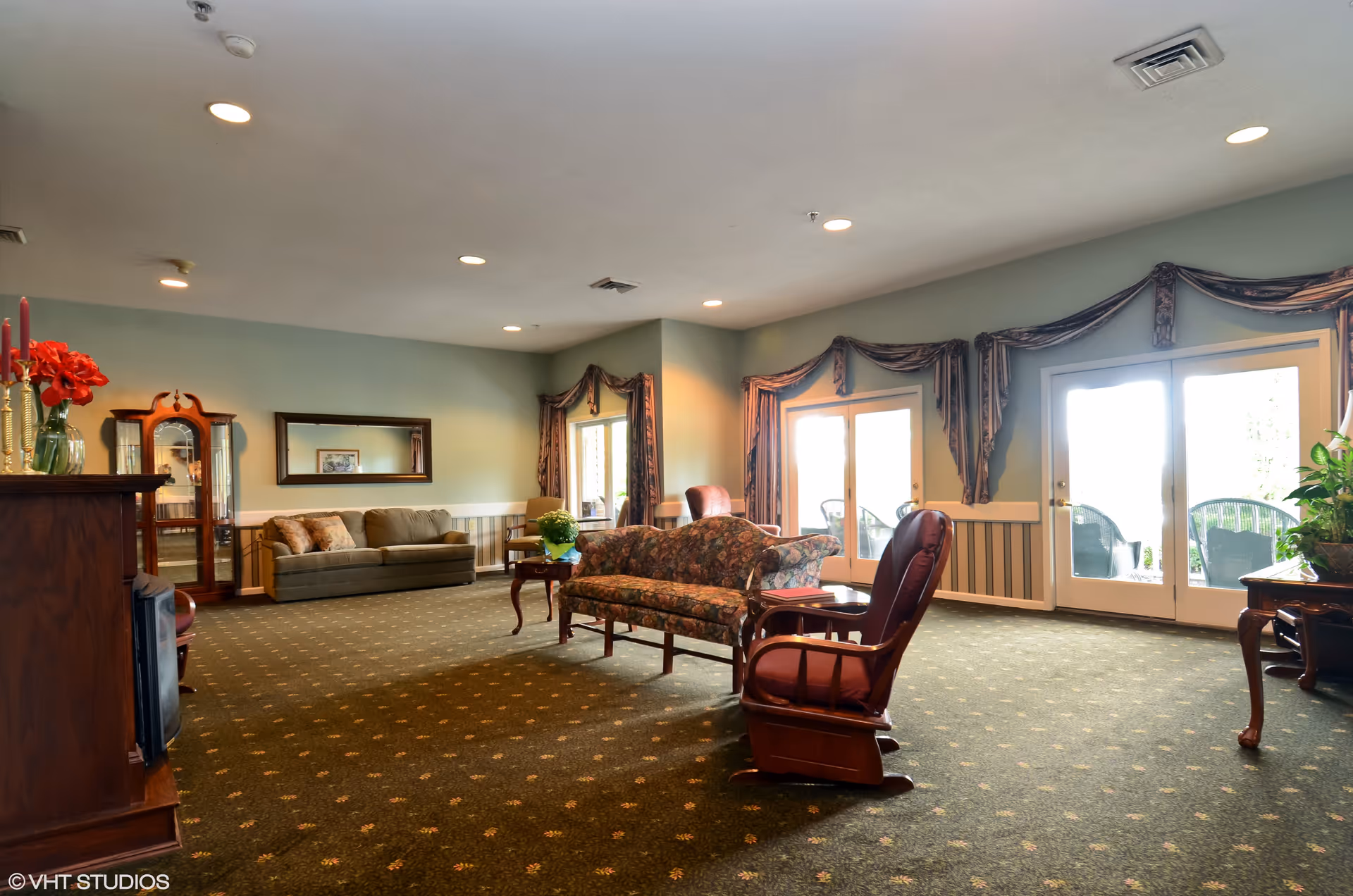 Spacious common room with sofas, armchairs, coffee table and glass doors leading to an outdoor patio.