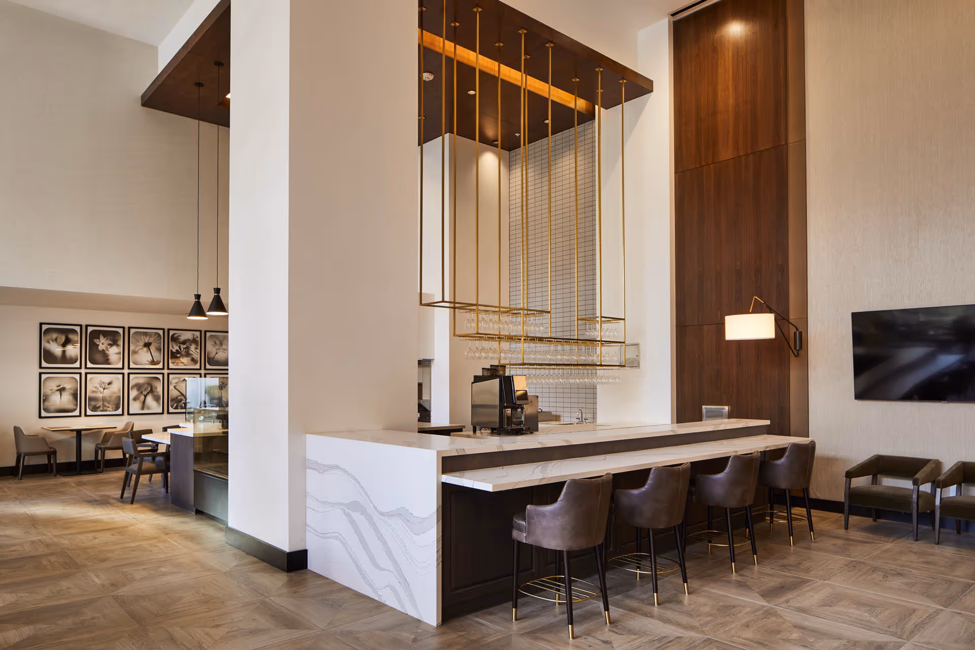 Modern communal bar and lounge area with a marble-topped counter, bar stools, seating, and a wall-mounted TV.