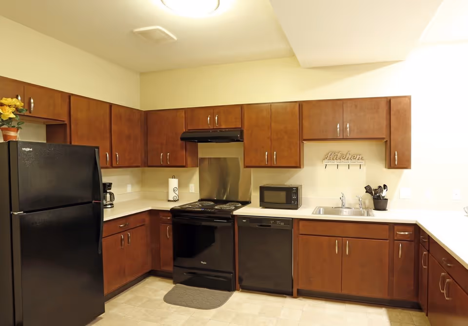 Modern kitchen with dark wood cabinets, black refrigerator, stove, dishwasher and microwave, and a sink on light countertops.
