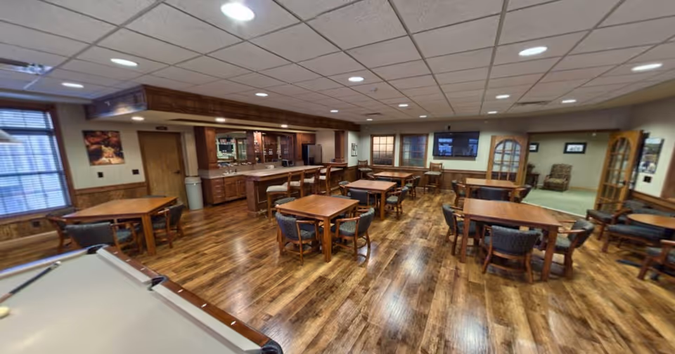 Spacious communal room with wooden tables and chairs, a bar area and a pool table on wood flooring.