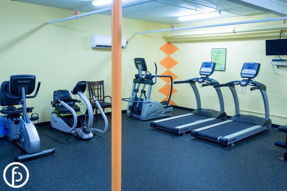 Small fitness room with treadmills, ellipticals, and stationary bikes against yellow walls.