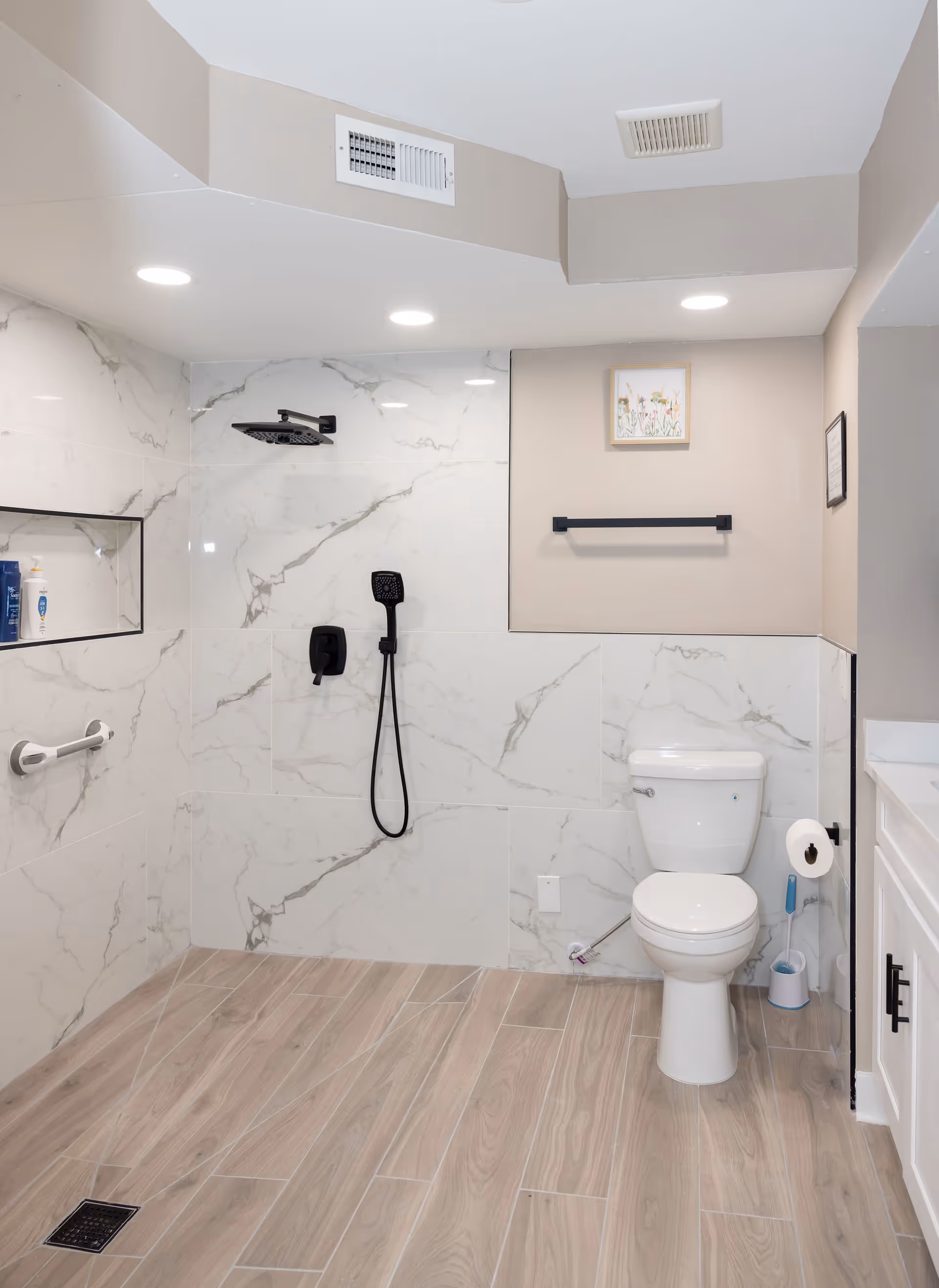 Accessible modern bathroom with a walk-in shower featuring a handheld and overhead shower head, a toilet, grab bar, and wood-look tile floor.