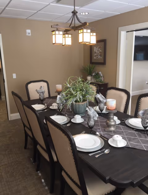 Formal dining room with a dark wooden table set for a meal, upholstered chairs, a plant centerpiece and a hanging light fixture.