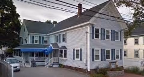 White multi-story residential building with a blue awning over the entrance and a parked car in the driveway.