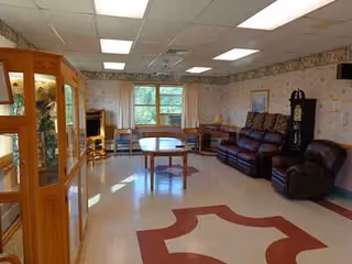 A cozy senior living common area with leather seating, tables, and display cabinet.