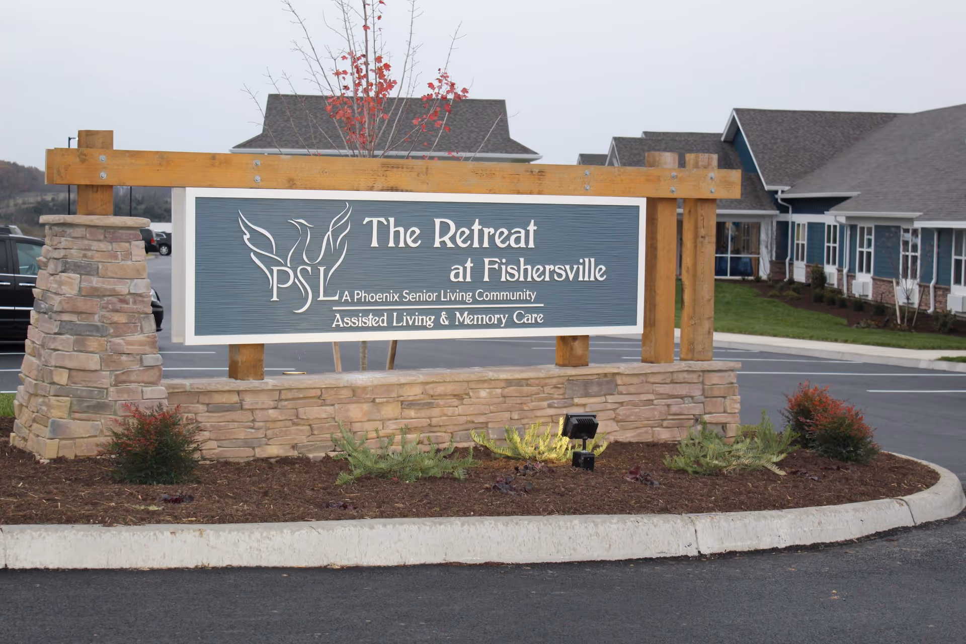 Outdoor view of a large sign for The Retreat at Fishersville, a Phoenix Senior Living Community offering Assisted Living & Memory Care, with buildings and parking lot in the background.