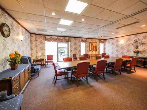 A conference-style dining room in a senior facility with red chairs around a long table.