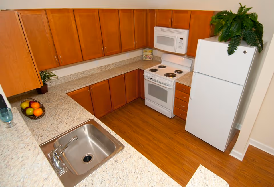 U-shaped kitchen with wood cabinets, laminate countertops, a stainless sink, white stove and microwave, and a white refrigerator.