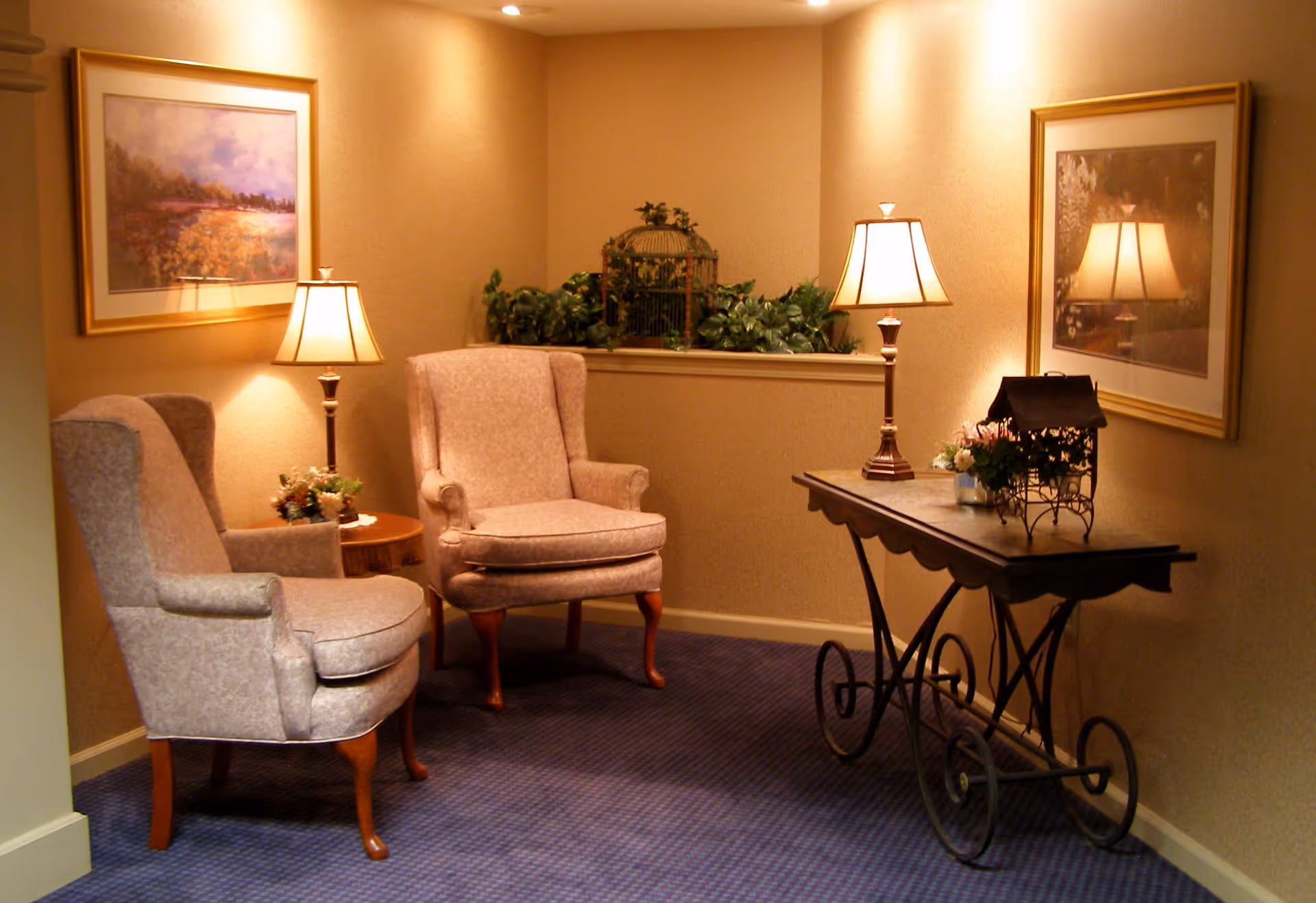 Warmly lit sitting area with two upholstered armchairs, table lamps, a side table and decorative console against a beige wall.