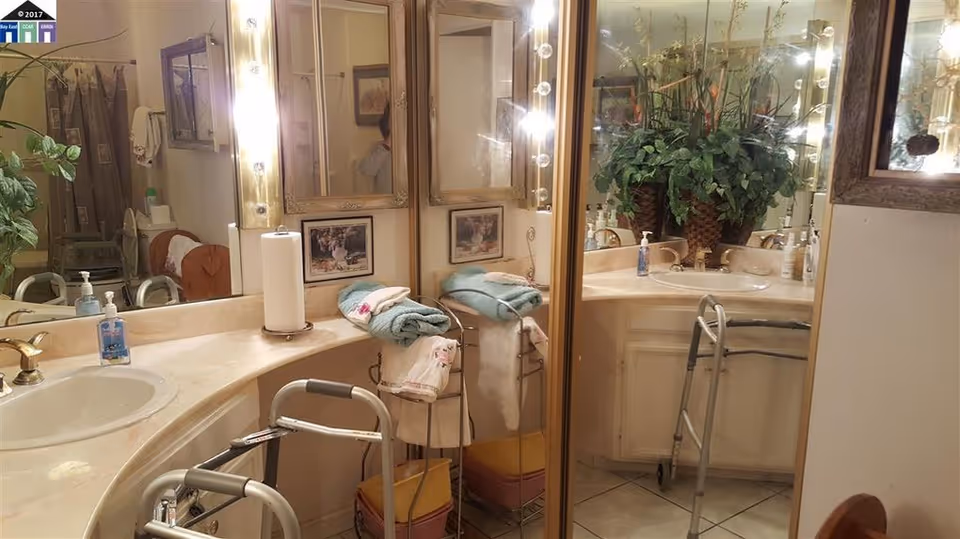 Bathroom vanity with double sinks, mirrored cabinets, a walker, towels and a potted plant.