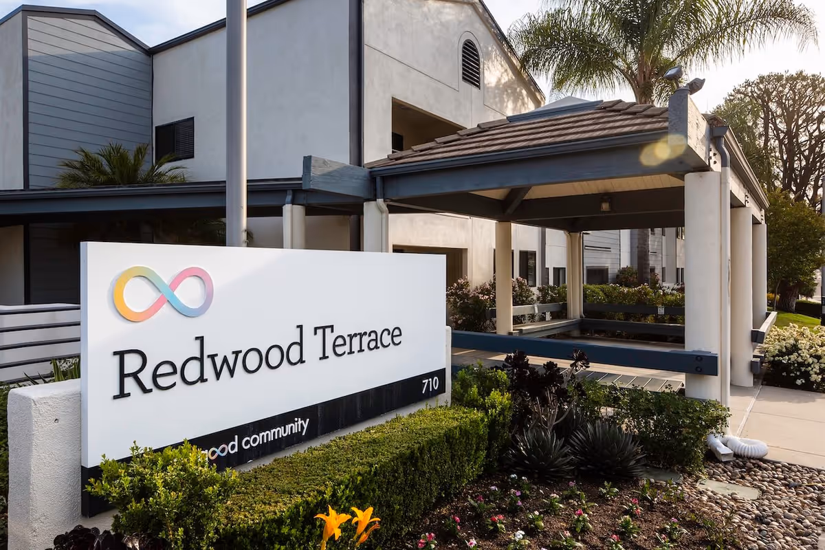 Sign reading 'Redwood Terrace' in front of a covered entry and landscaped grounds of the building.