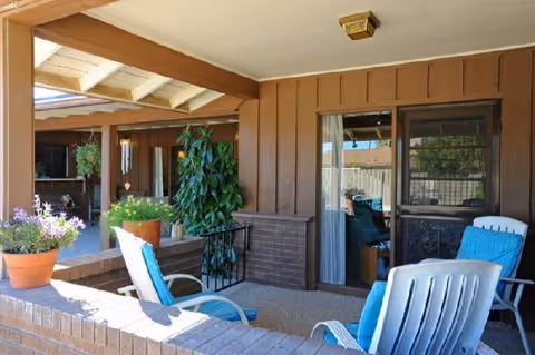 Covered outdoor patio of a senior living home with blue chairs and potted plants.