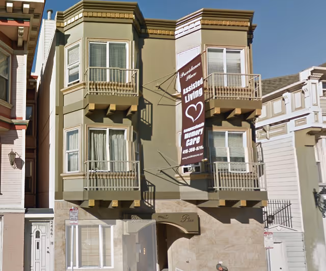 Front facade of a three-story assisted living building with a vertical banner reading 'Assisted Living' and 'memory care'.