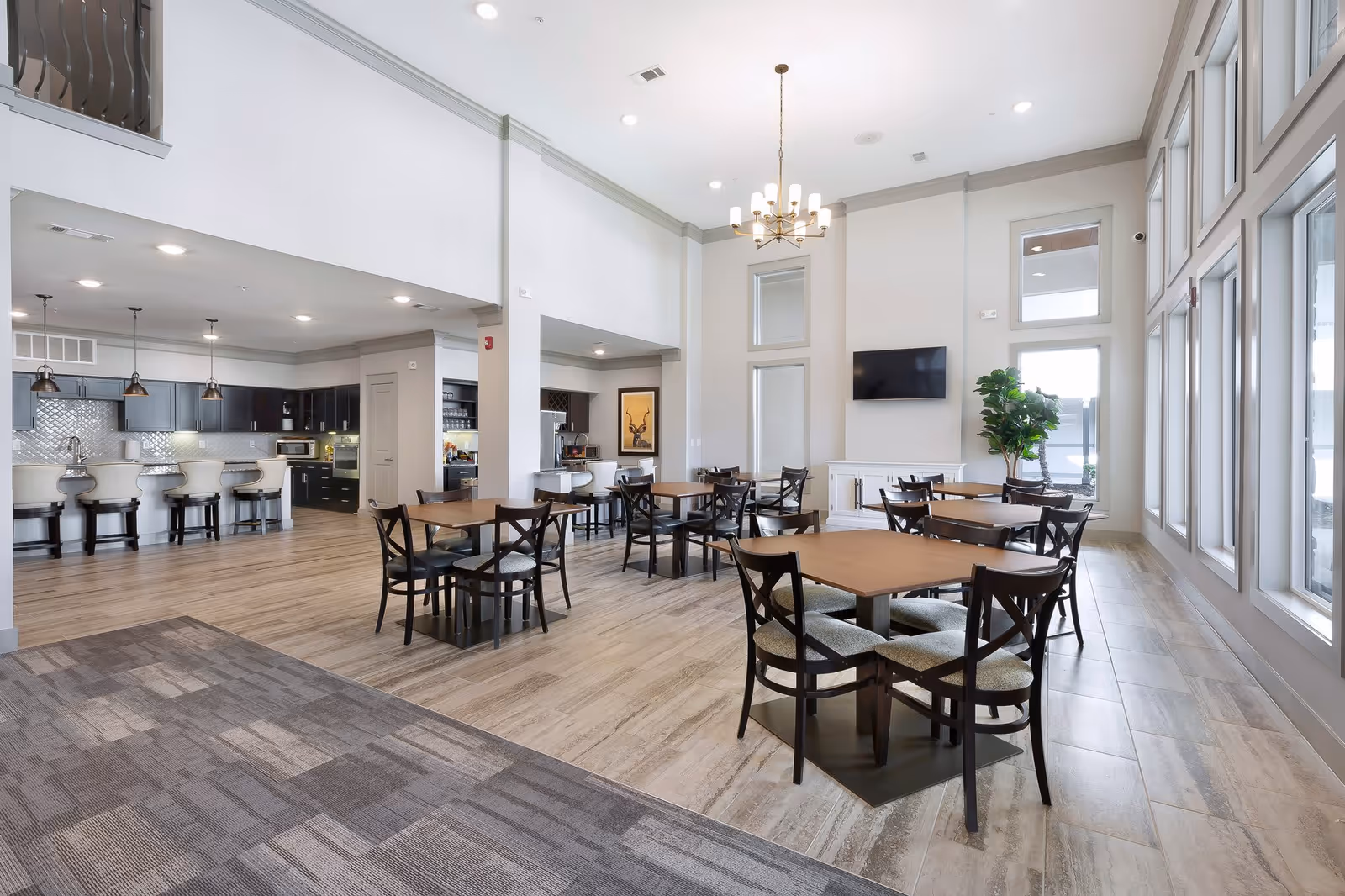 Spacious bright dining and lounge area with multiple tables and chairs, a kitchen bar, high ceilings, and large windows.