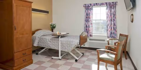 A patient room with bed, wooden armoire, window with purple curtains, and two chairs.