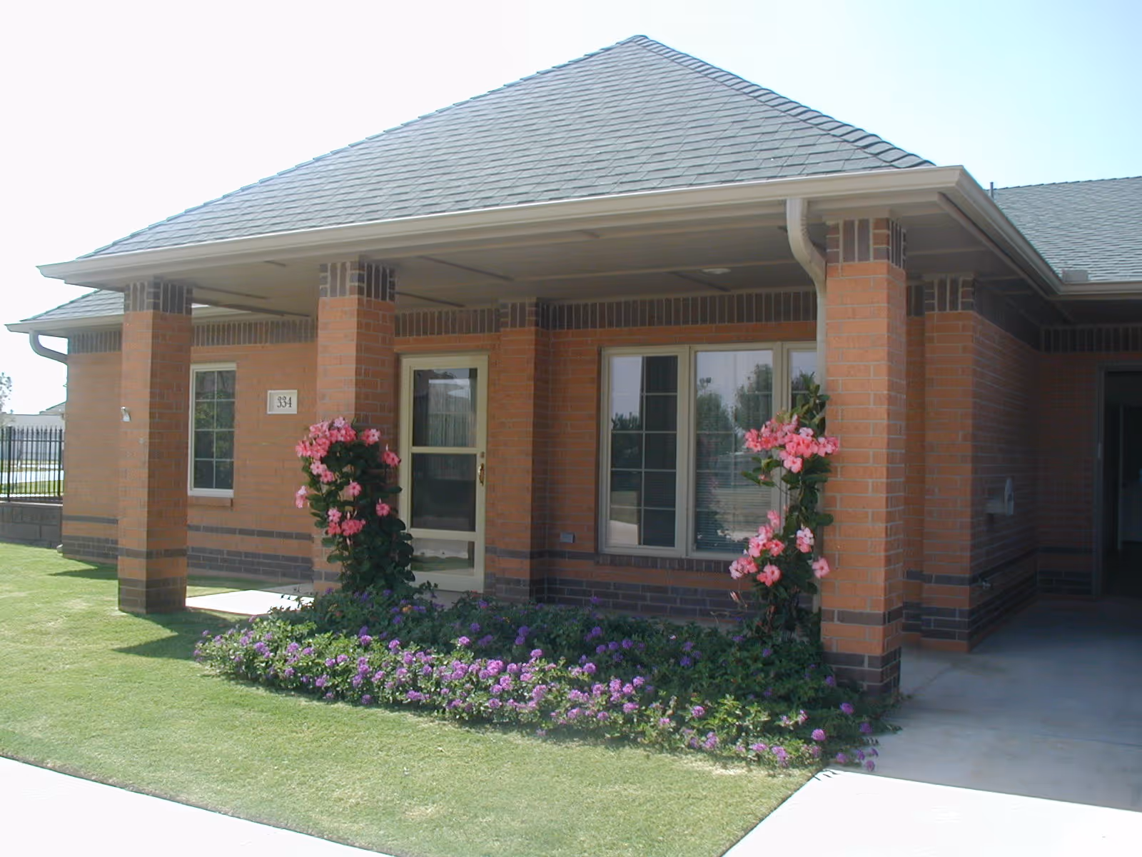 Front entrance of a single-story brick building with a covered porch, columns, and flower beds.