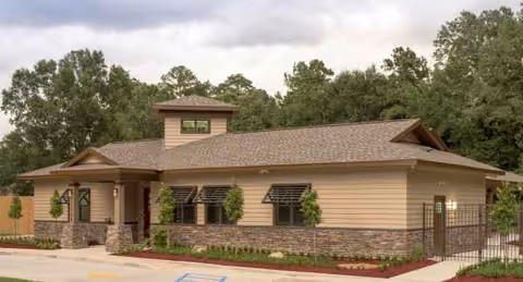 Single-story beige building with stone base, front entrance, and small trees.