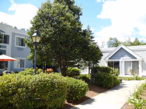 Exterior view of The Meadows facility with a walkway, trees, hedges, and outdoor seating.
