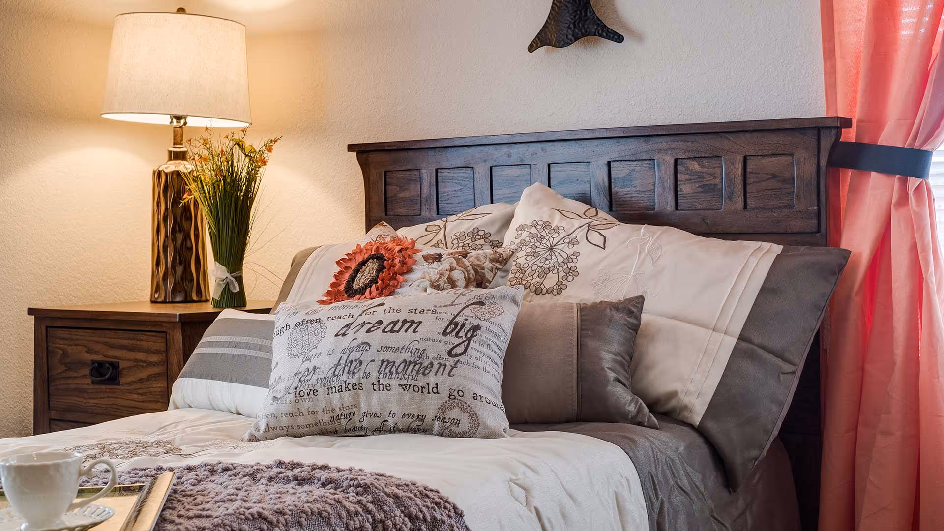 A neatly made bed with decorative pillows, a wooden headboard, bedside lamp and nightstand in a softly lit bedroom.