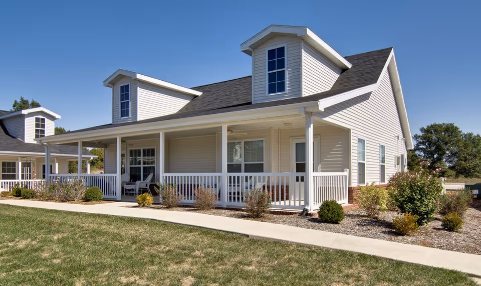 White, single-story senior living facility with a wraparound porch and well-kept landscaping.
