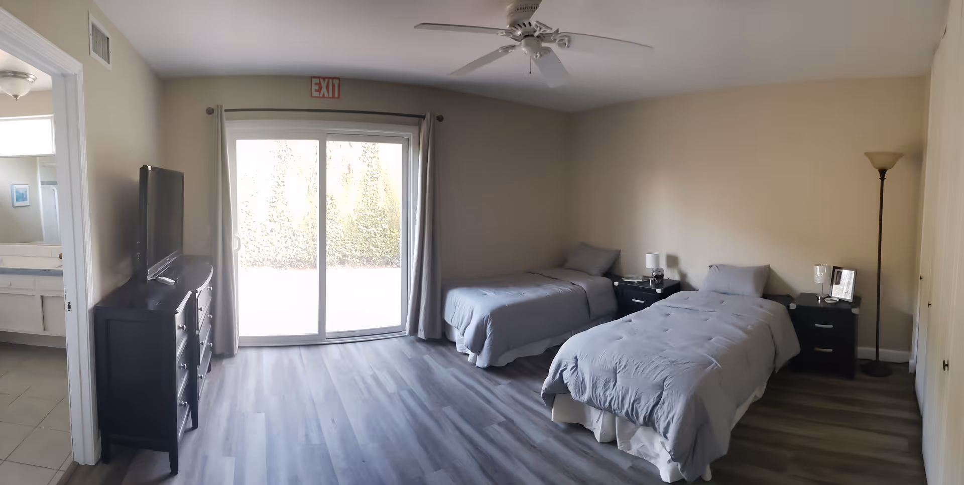 Spacious bedroom with two twin beds, a sliding glass door, TV on a dresser, and an adjacent bathroom.