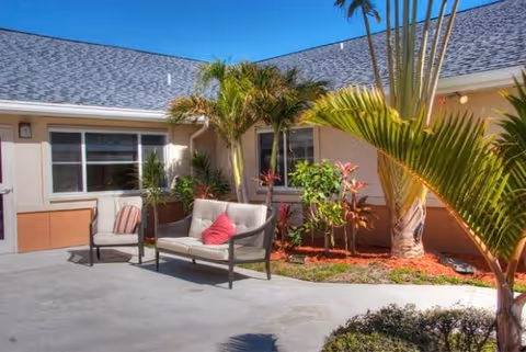 Outdoor courtyard with palm trees, cushioned seating, and a beige building facade.