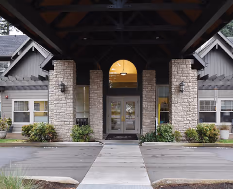 Covered entrance of a single-story building with stone columns, double glass doors, and landscaping.