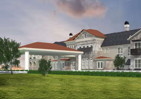 Exterior view of a large multi-story senior living building with a covered porte-cochère entrance, arched windows, and a grassy foreground.