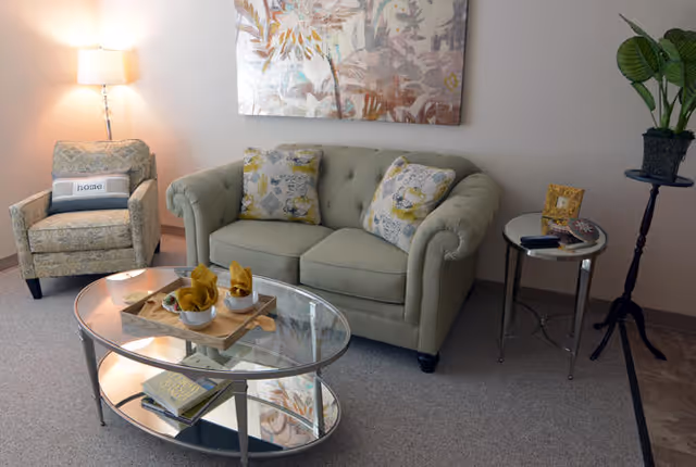 A cozy sitting area with a loveseat, armchair, glass coffee table, floor lamp and wall art.
