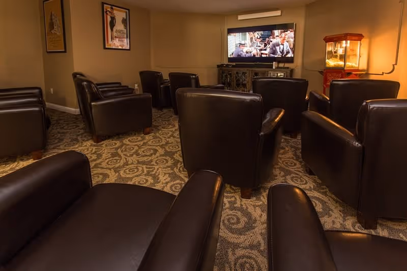 Small theater-style room with rows of leather armchairs facing a wall-mounted TV and a popcorn machine.