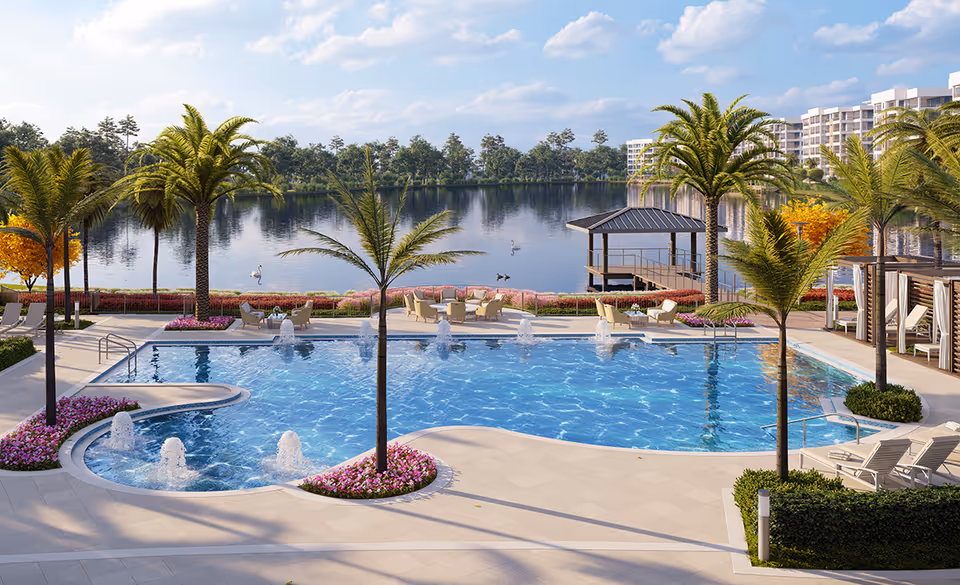 Resort-style outdoor swimming pool surrounded by palm trees, lounge chairs and fountains with a lake and waterfront gazebo in the background.