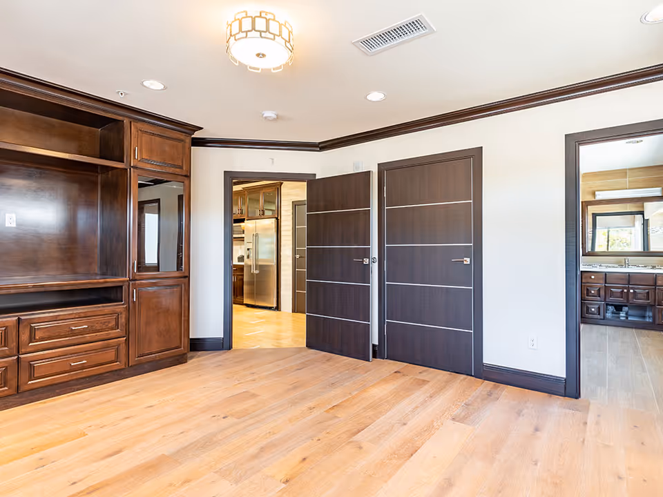 Interior room with built-in dark wood cabinetry, light hardwood floors, and two modern dark doors opening to a kitchen and bathroom.