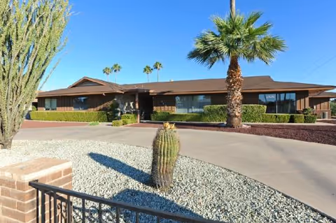 Single-story assisted living facility with desert landscaping, palm trees, and a curved driveway.