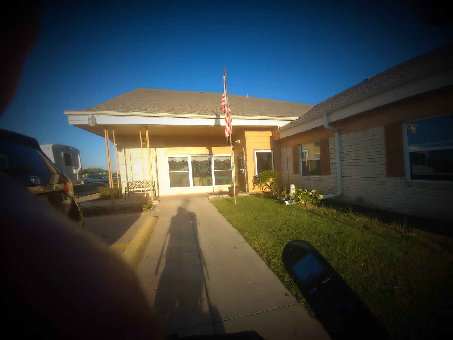 Front entrance of a one-story rehabilitation center with a sidewalk leading to glass doors and an American flag.