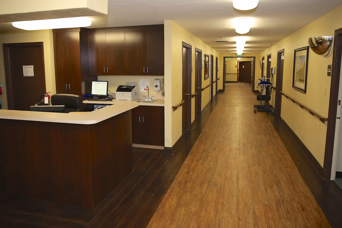 Long interior corridor with a nurses' station on the left and multiple resident room doors along the hallway.