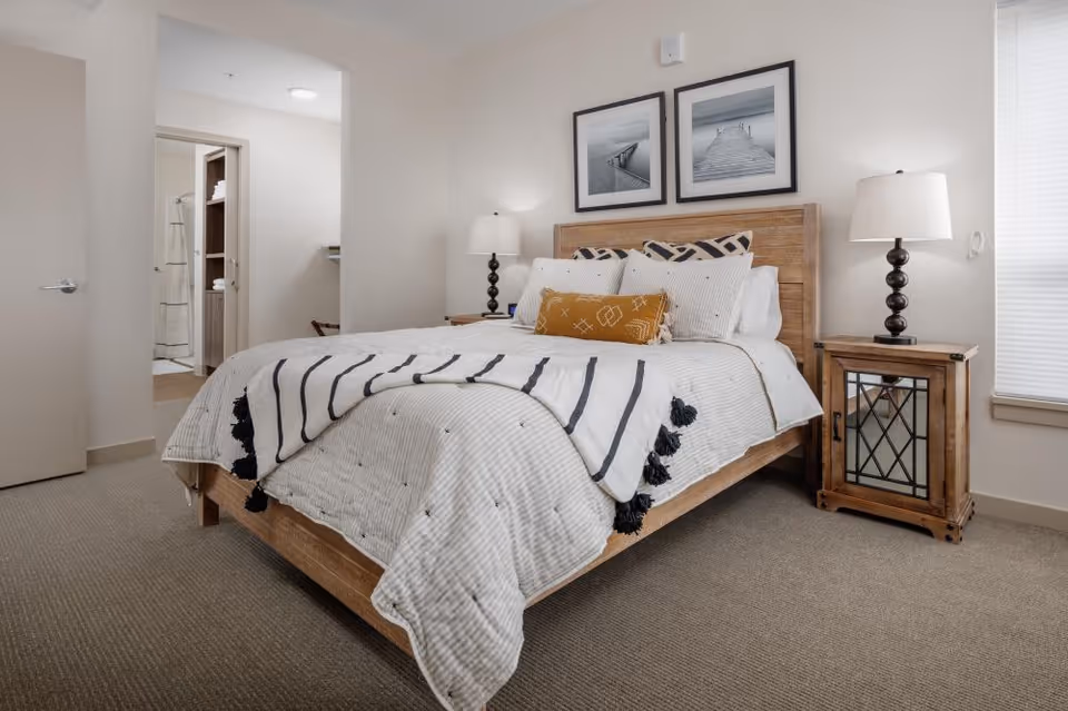 A neatly furnished bedroom with a wooden bed, striped bedding, two bedside lamps and a doorway to a bathroom.