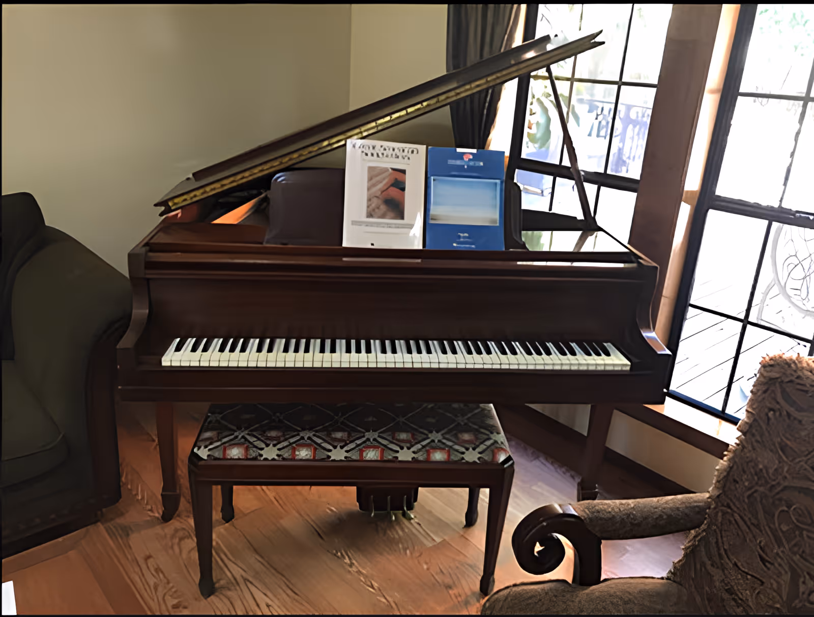 A grand piano with sheet music and a patterned bench sits near a window in a cozy living room.