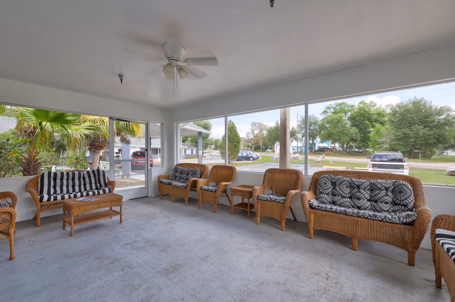 Enclosed sunroom with wicker sofas and chairs, a ceiling fan, and large windows overlooking the street.