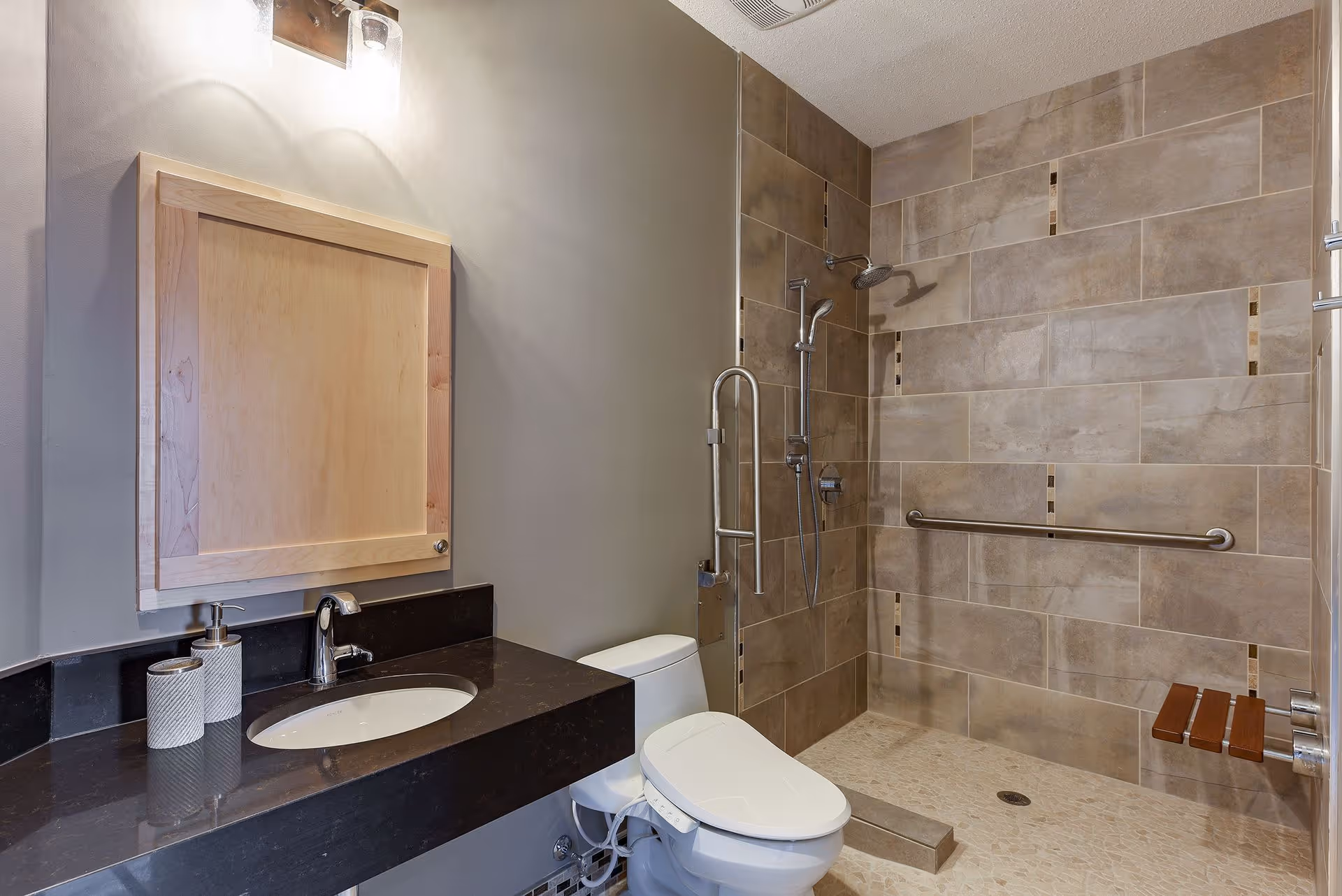 Accessible bathroom featuring a sink vanity, toilet, and a roll-in tiled shower with grab bars and a folding seat.