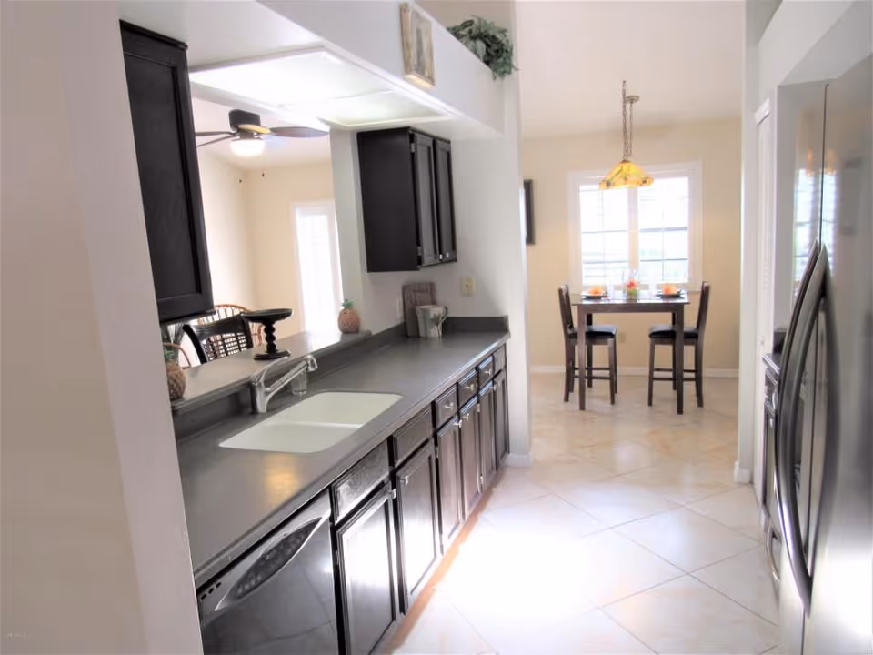 Bright kitchen interior with dark cabinets, a sink and countertop leading to a small breakfast nook with a table and chairs.
