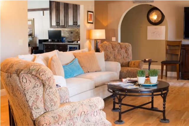 Comfortable living room with a beige sofa, patterned armchairs, a round coffee table and hardwood floors.