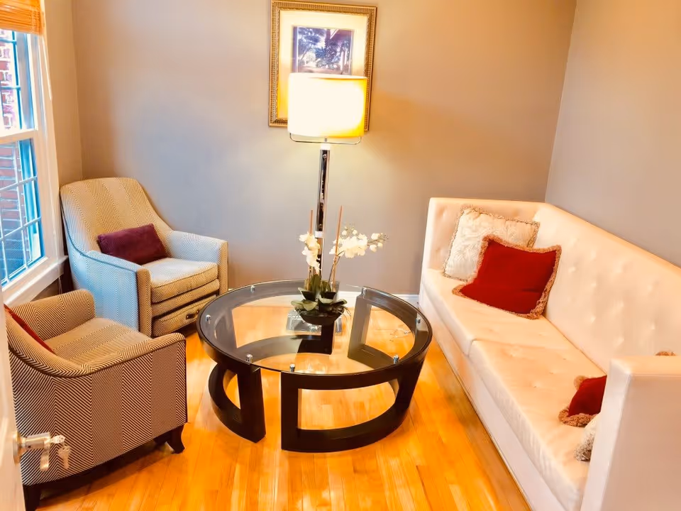 Bright living room with a white tufted sofa, two upholstered armchairs, a round glass coffee table and a floor lamp.