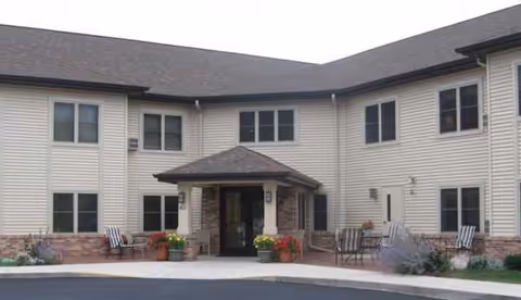 Two-story beige assisted living building with a central entry and benches at the entrance.
