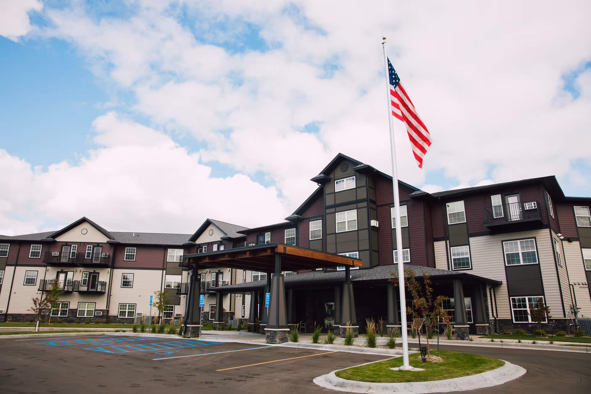 Front exterior of a multi-story senior living building with a covered entrance and an American flag in front.