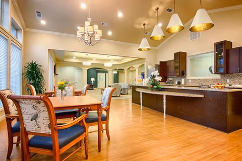 Bright communal dining area with wooden tables and upholstered chairs adjacent to a large open kitchen and breakfast bar.